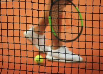 Person wearing a pair of white top sneakers while holding a Wilson tennis racket Photo by John Fornander on Unsplash