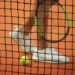 Person wearing a pair of white top sneakers while holding a Wilson tennis racket Photo by John Fornander on Unsplash